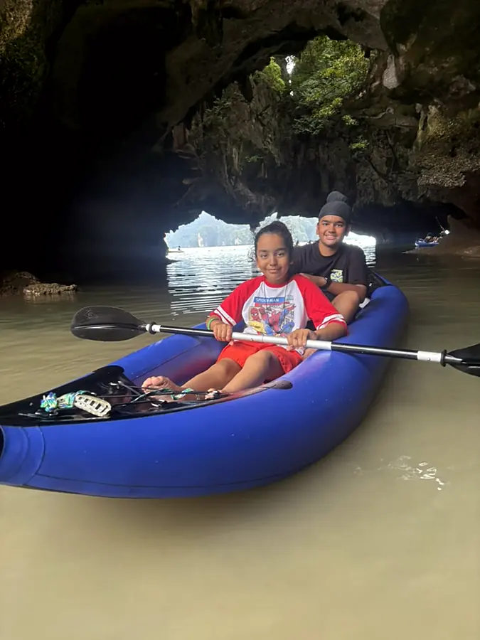 Two young paddlers in a blue kayak inside a sea cave, daylight in the arch behind them