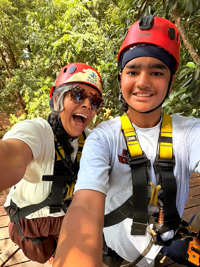 A grinning selfie in zipline helmets and harnesses, green jungle behind
