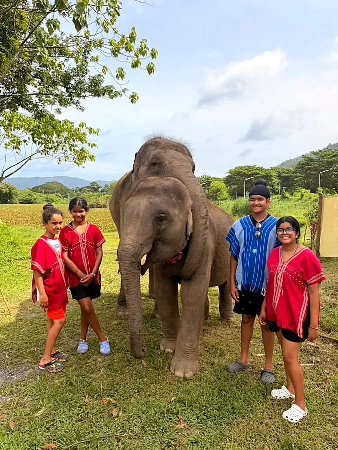 Four of the kids in red and blue woven shirts standing either side of an elephant on grass