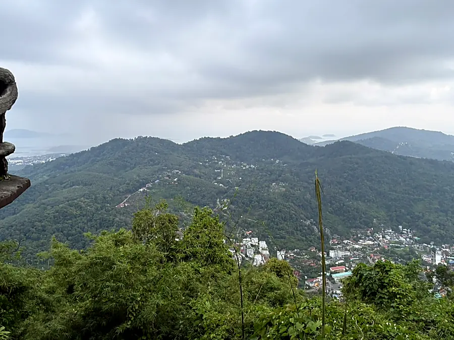 Green hills rolling down toward Phuket town and the sea under heavy cloud