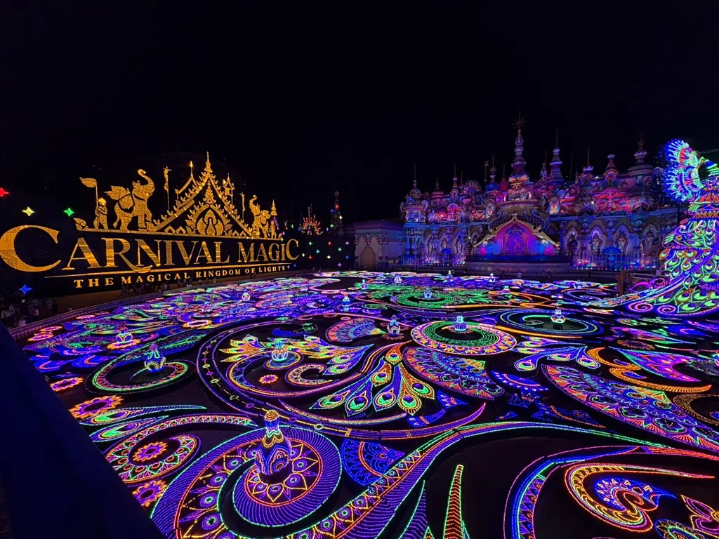 An enormous plaza covered in neon peacock-feather light patterns at night