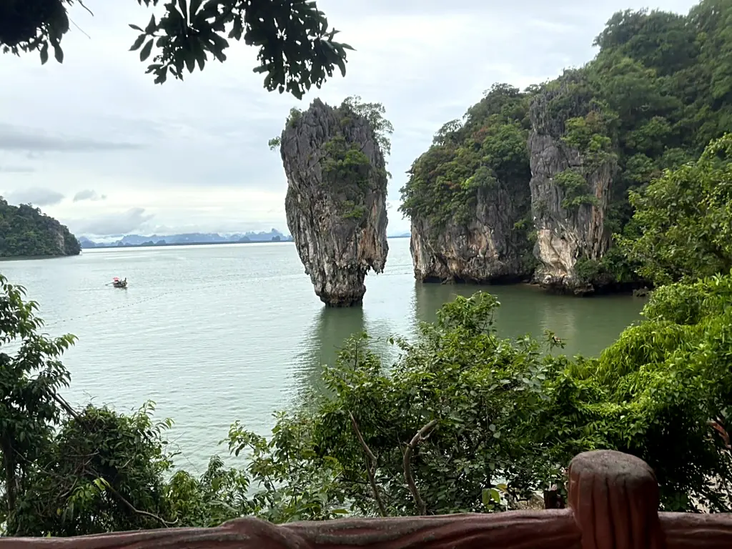 Ko Tapu, a narrow limestone spire rising out of jade water, framed by jungle and a longtail boat passing behind